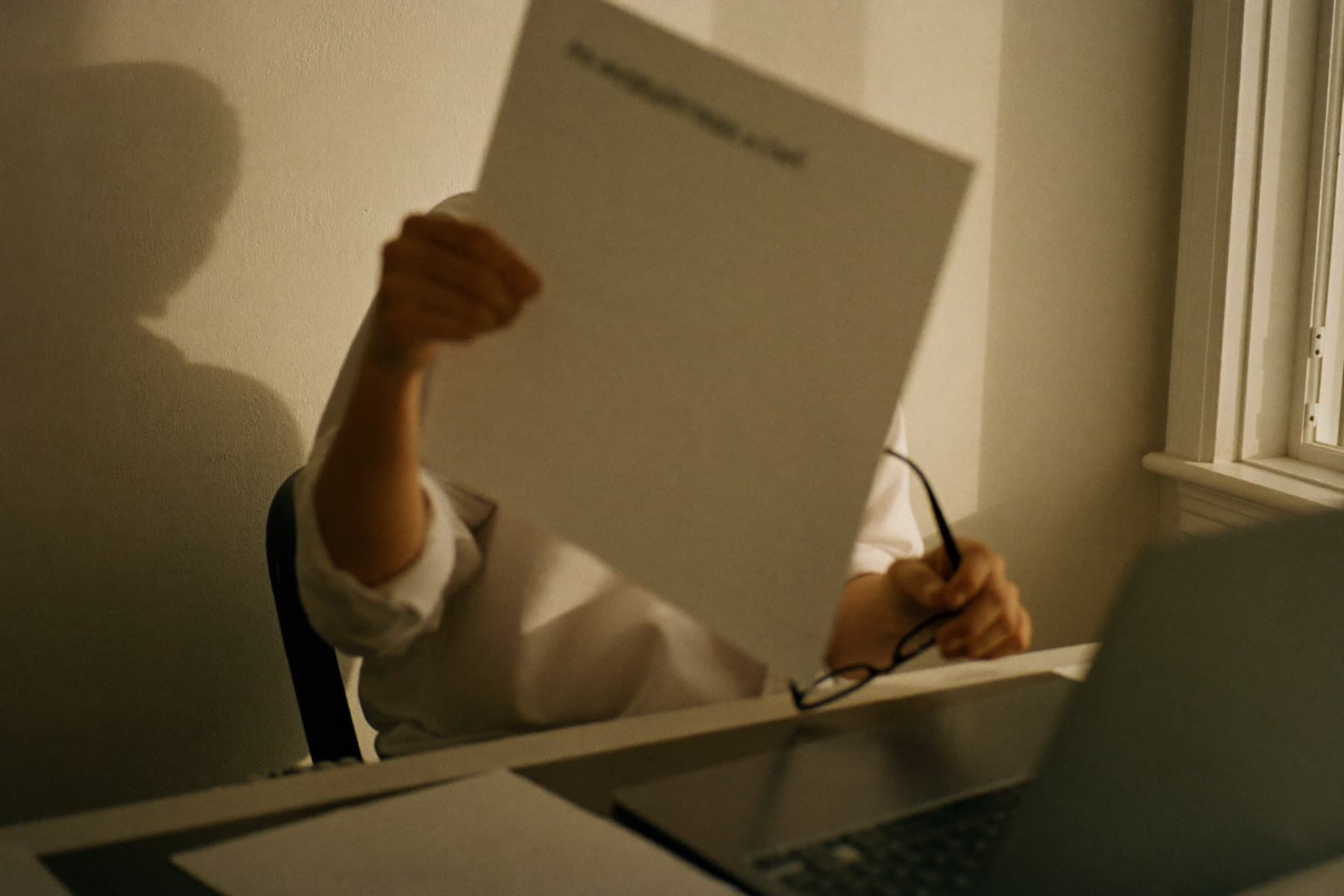 A professional reading a report at a desk by a tall window